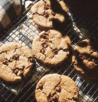 Chocolate chip cookies on a cooling rack with sunlight casting shadows