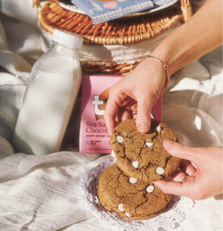 Person holding a cookie with a bottle of milk and a bag of cookies in the background.